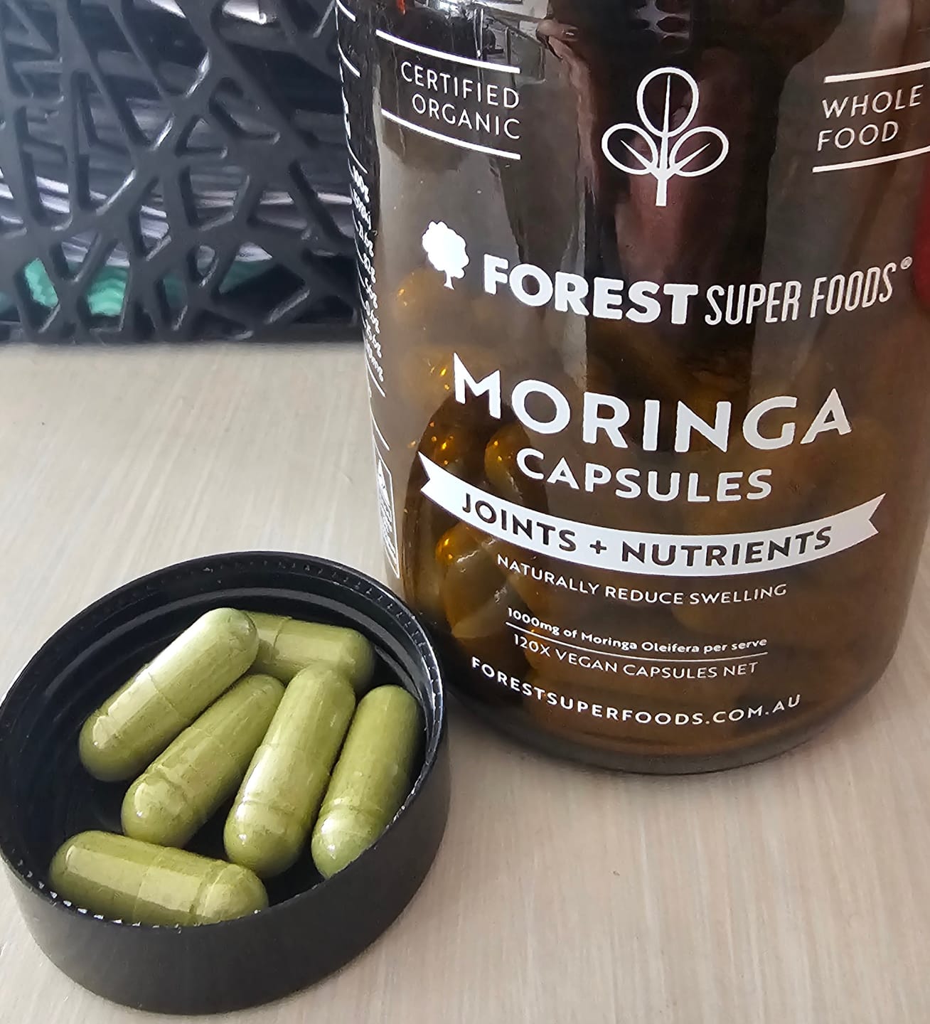 Open bottle of Forest Super Foods Organic Moringa Capsules showing green whole-leaf moringa capsules.